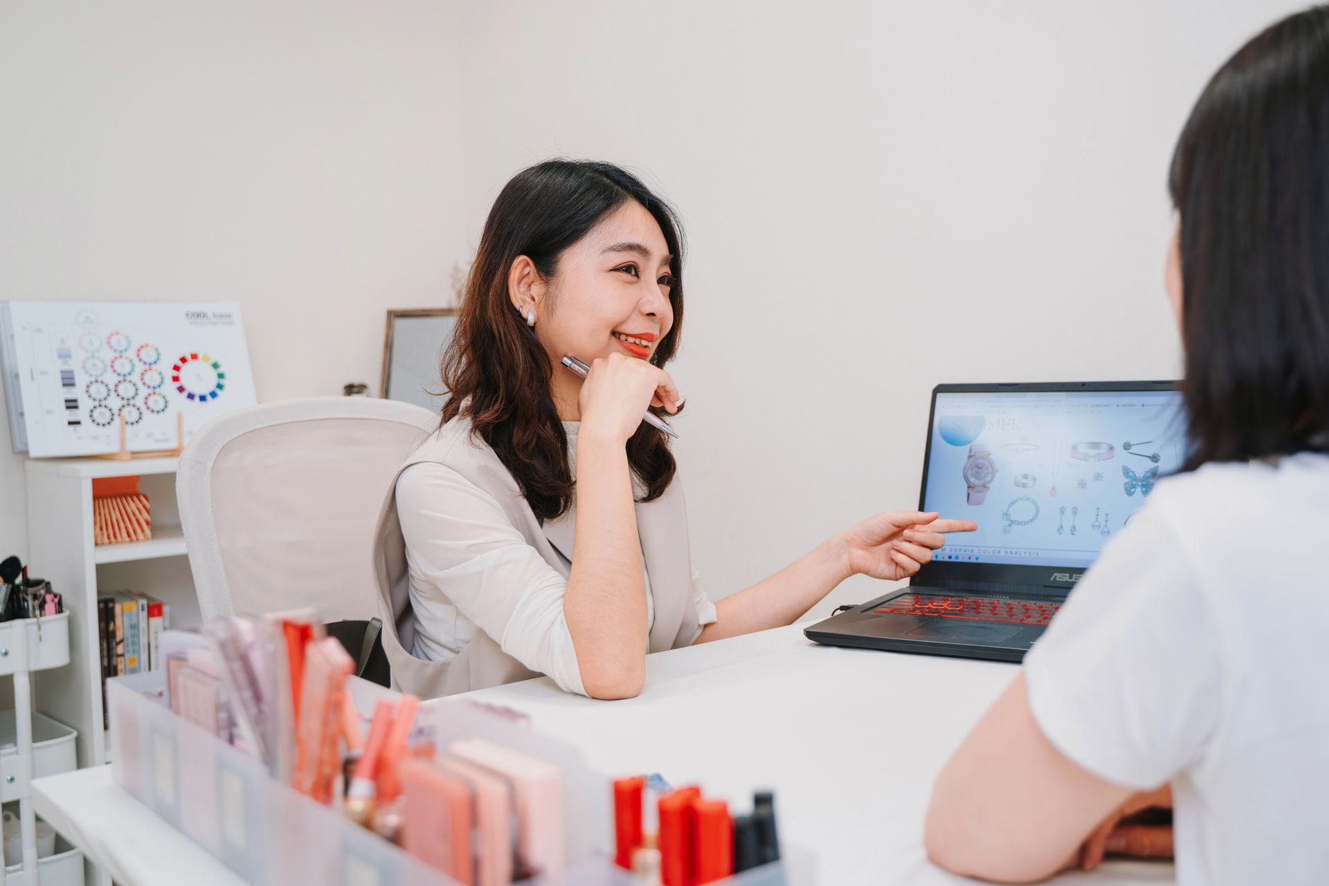 一位女士拿著筆記型電腦坐在桌旁，正在與另一位女士交談。