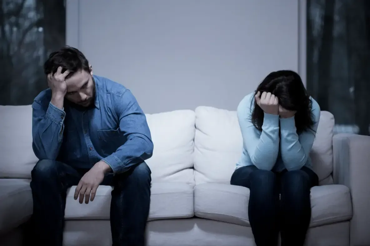 A man and a woman are sitting on a couch with their heads in their hands.