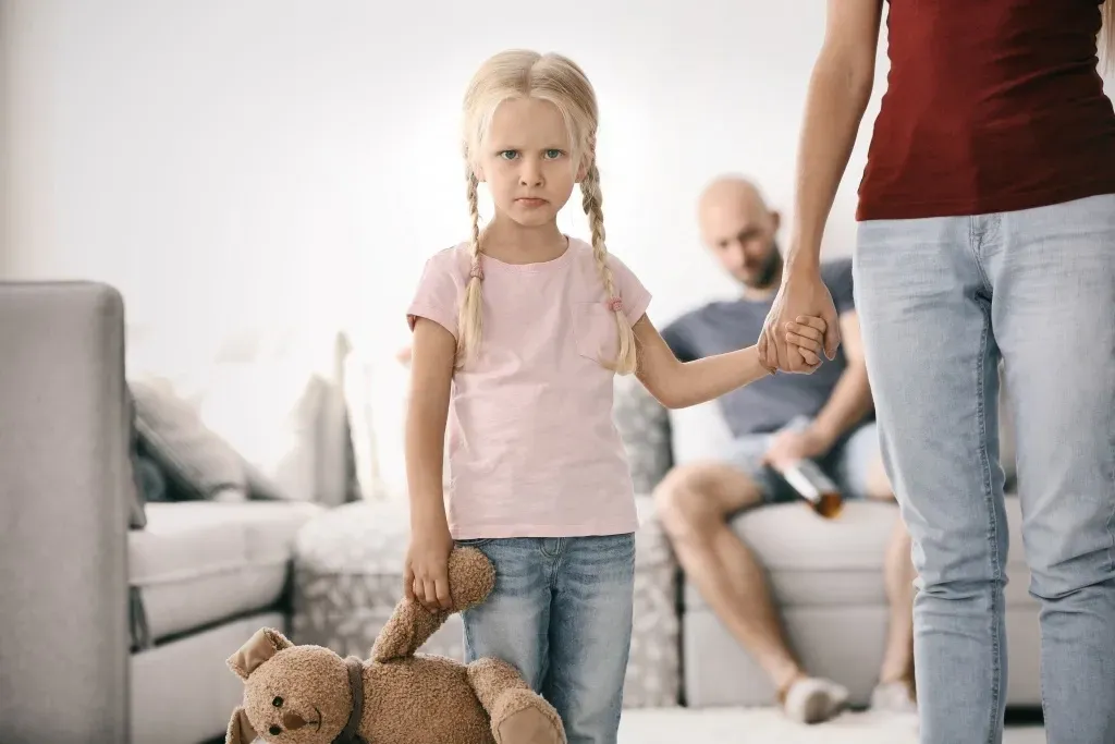 A little girl is holding a teddy bear while holding hands with her parents.
