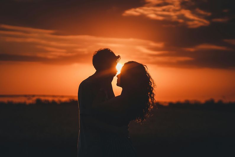 A man and a woman are kissing in front of a sunset.