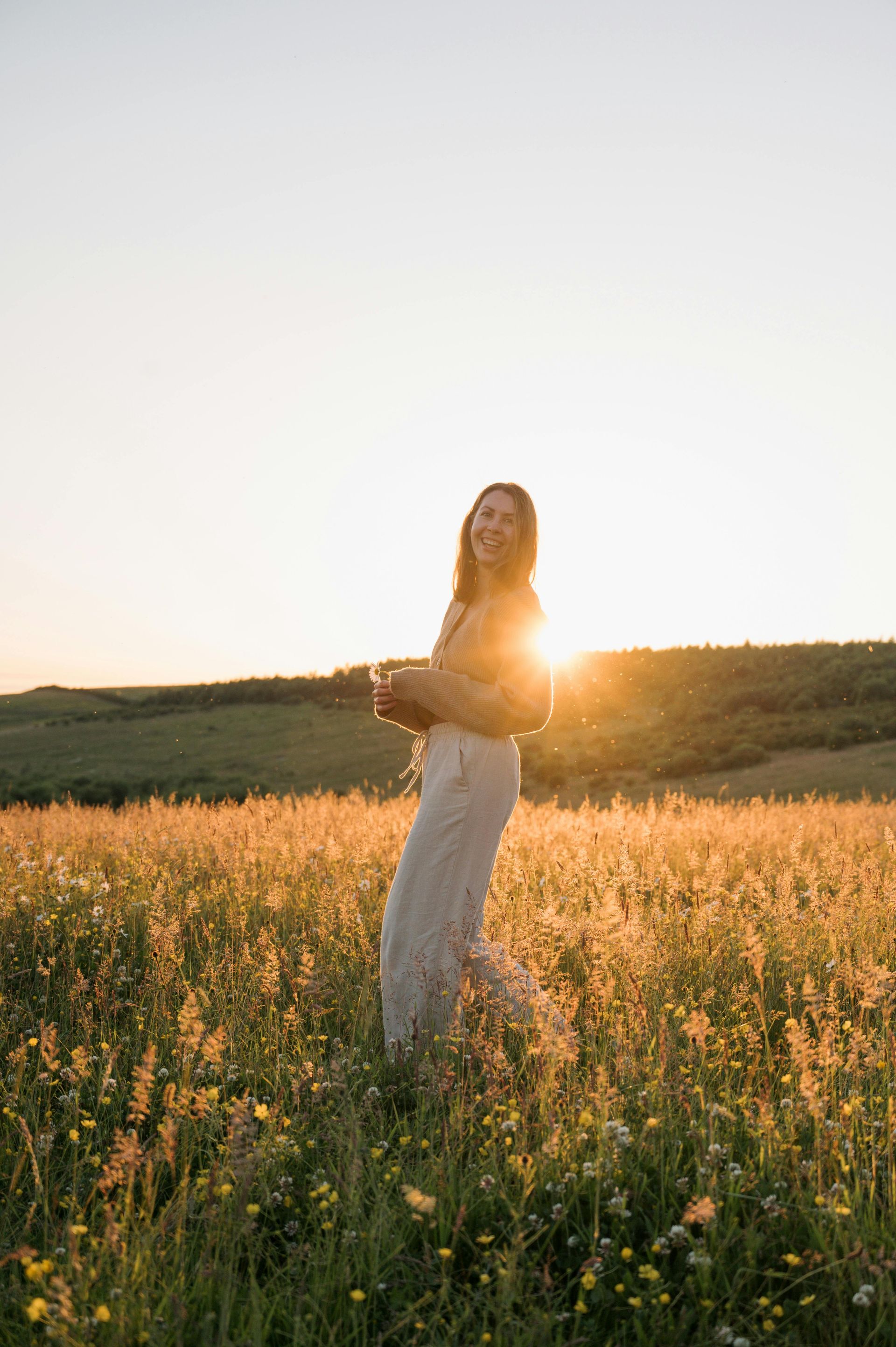 A woman is standing in a field of flowers at sunset.