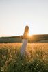A woman is standing in a field of flowers at sunset.