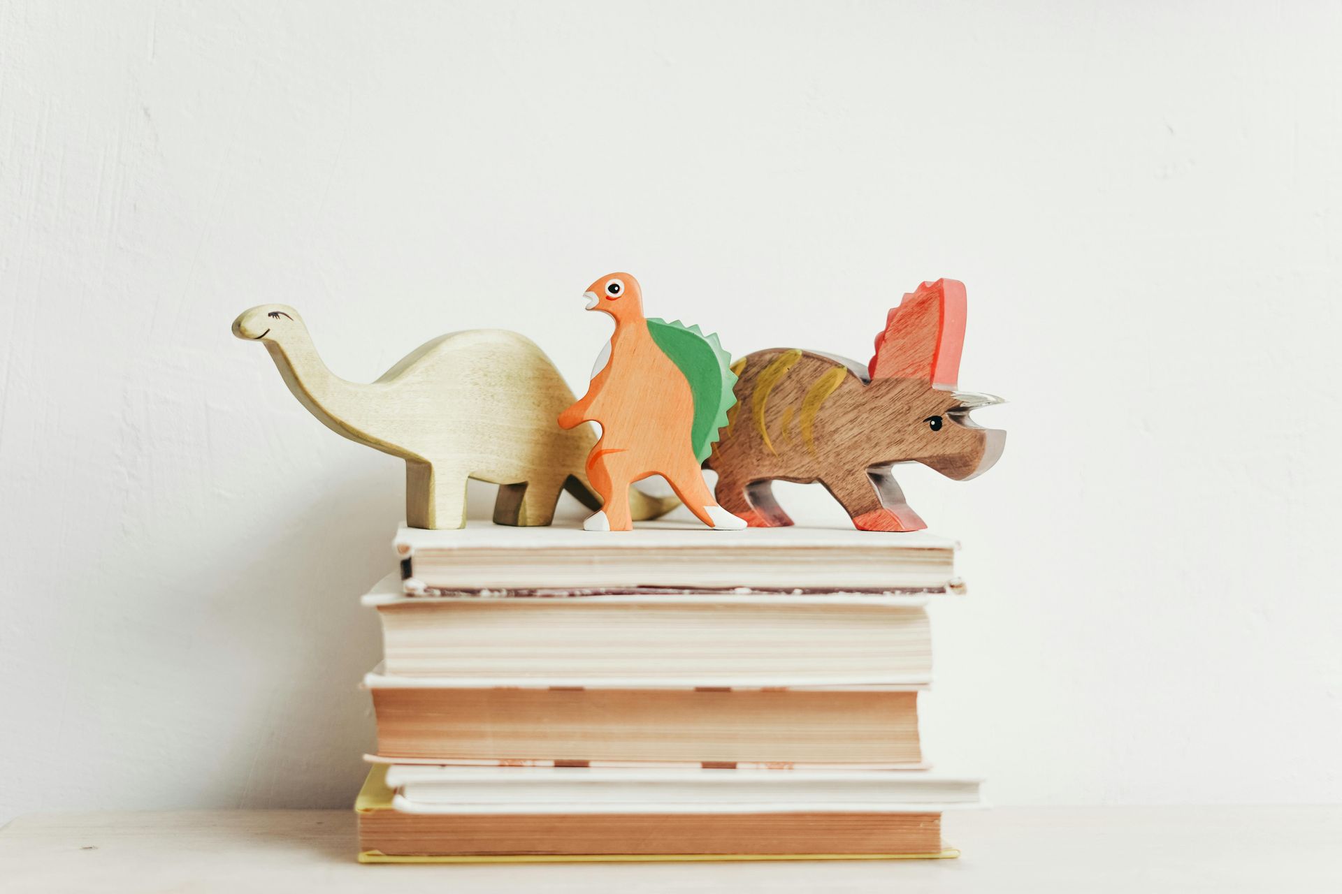 Three wooden dinosaurs are sitting on top of a stack of books.