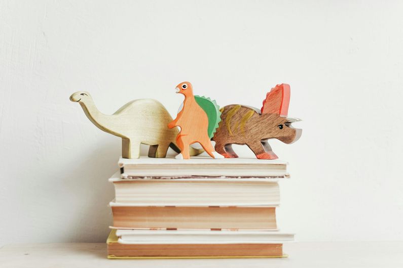 Three wooden dinosaurs are sitting on top of a stack of books.