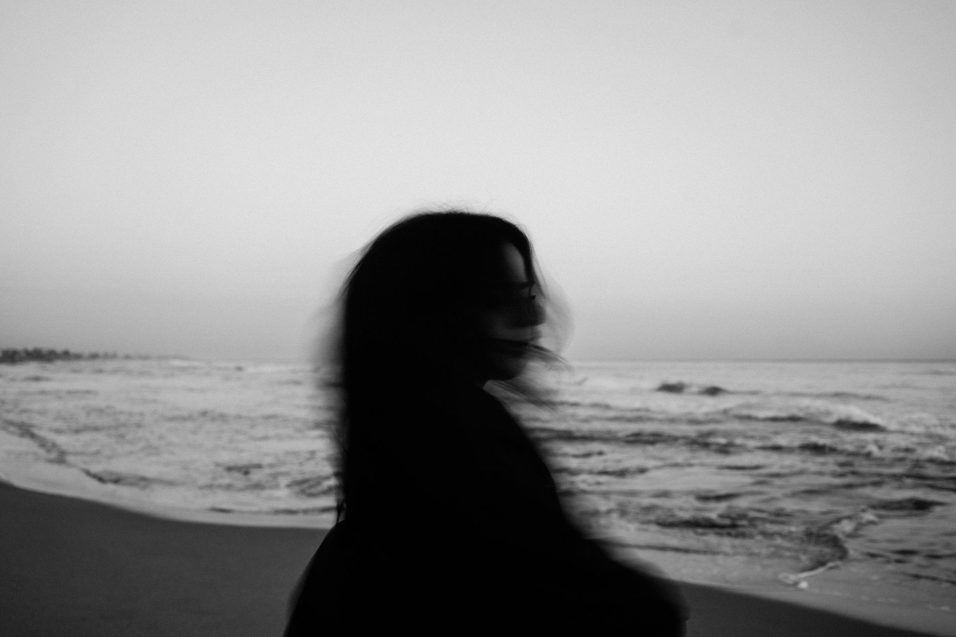 A black and white photo of a woman standing on a beach.