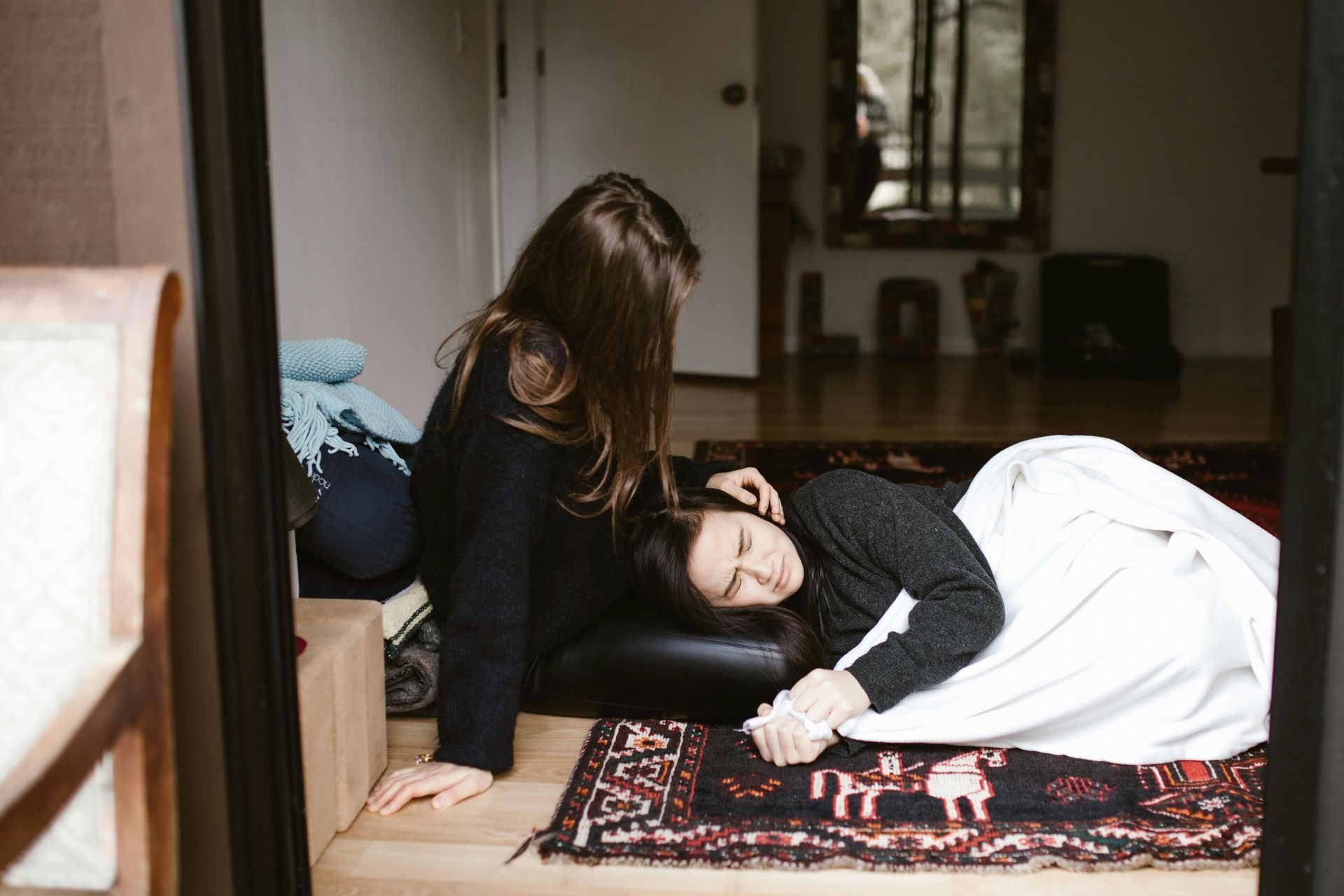 A woman is laying on the floor next to another woman who is laying on a couch.