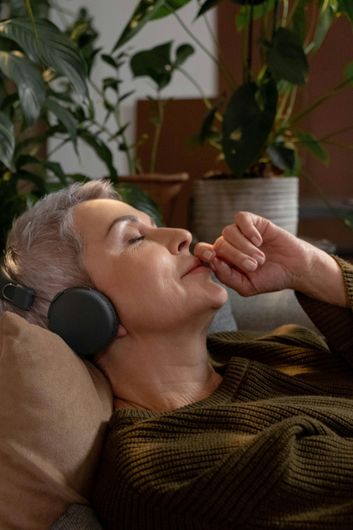 An older woman is laying on a couch wearing headphones.