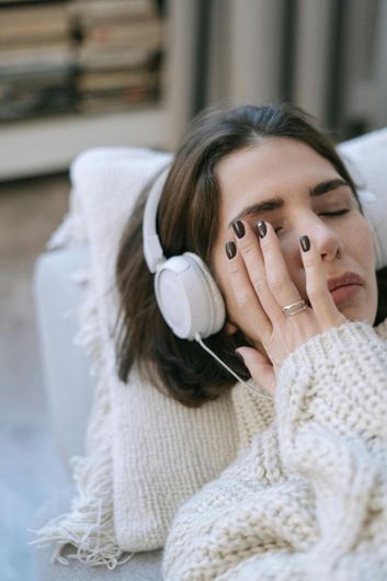 A woman is laying on a couch wearing headphones.