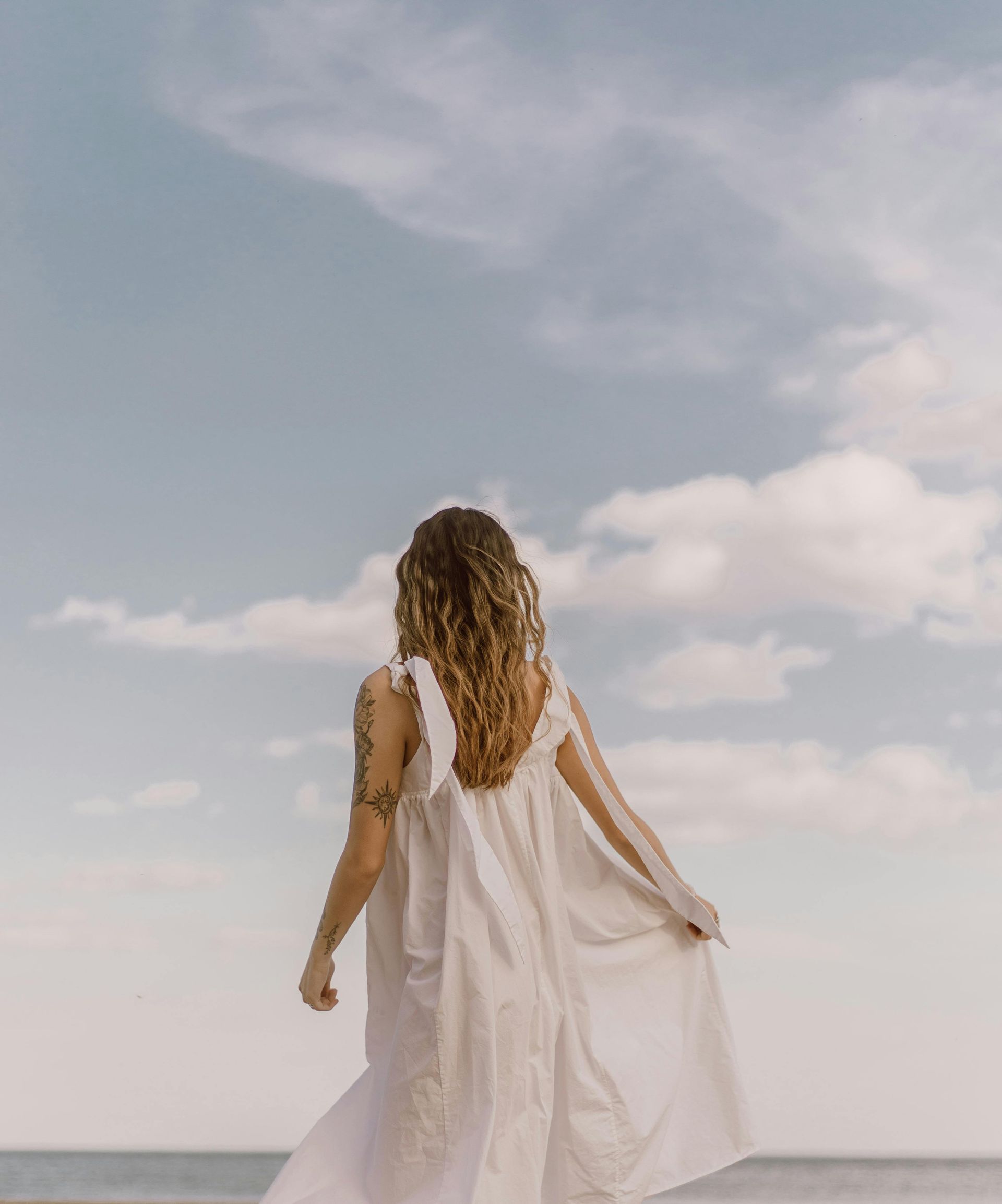 A woman in a white dress is walking on the beach.
