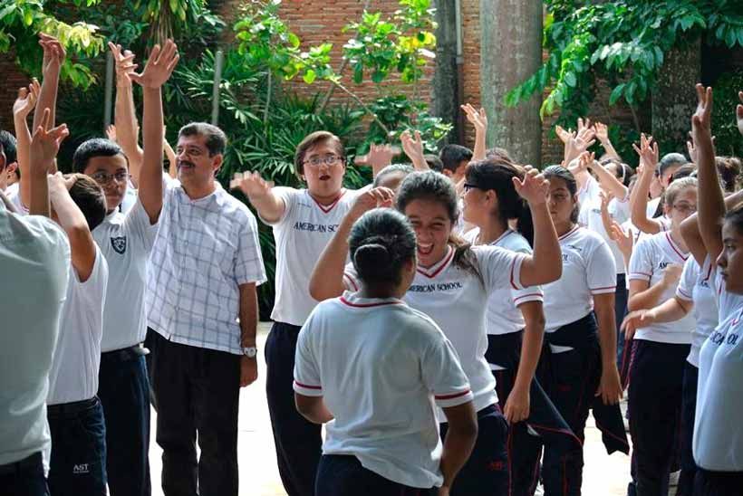 Un grupo de personas vestidas con camisas blancas, de pie al aire libre con los brazos en alto, aparentemente animando o participando.