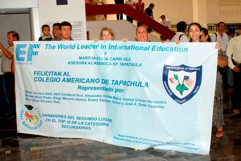 Un grupo de personas sostiene una pancarta blanca felicitando al Colegio Americano de Tapachula por ganar un concurso organizado por EF.