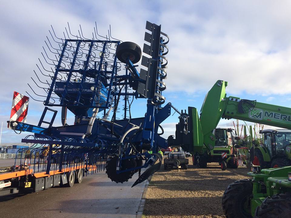A large blue tractor is being lifted by a green crane.