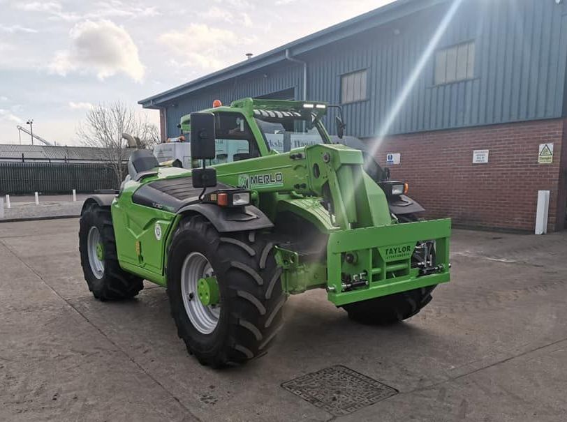 A green forklift is parked in front of a building.