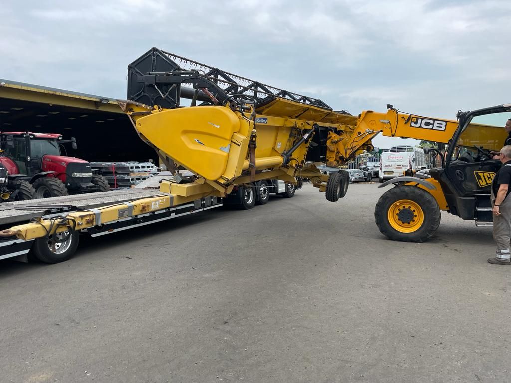 A man is standing next to a yellow tractor on a trailer.