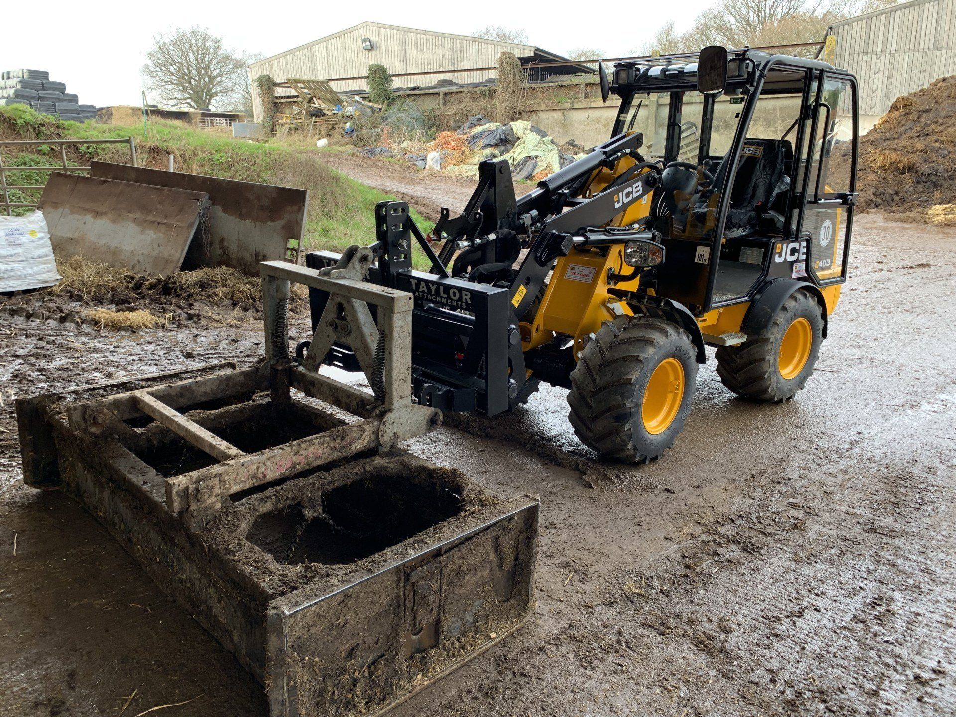 A yellow and black tractor is parked in the mud next to a wooden box.