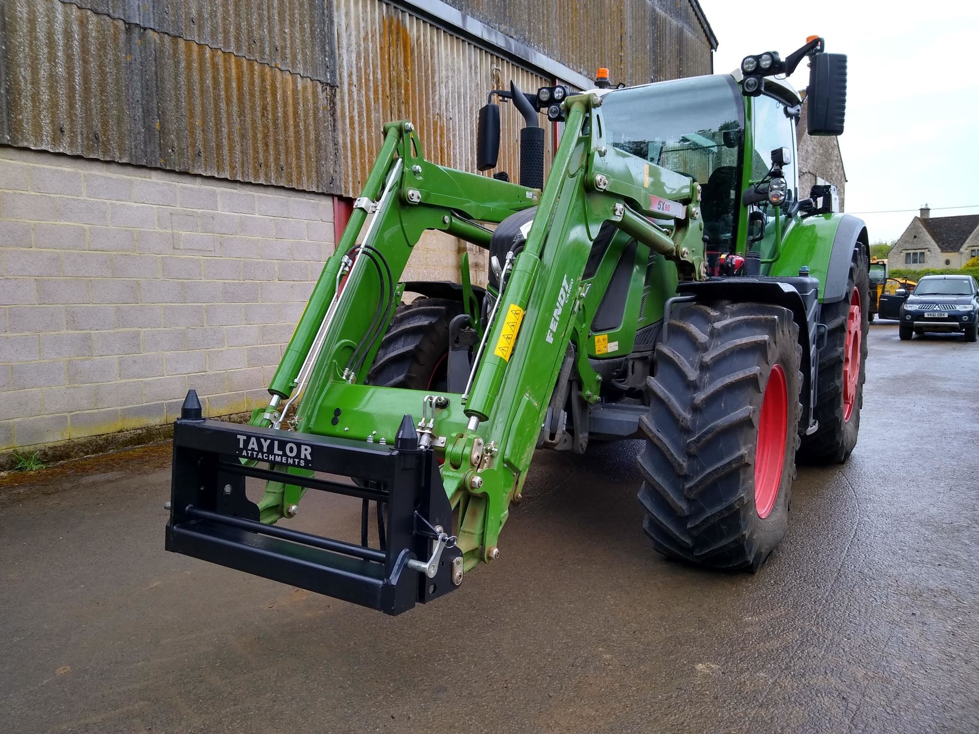 A green tractor is parked in front of a brick building.