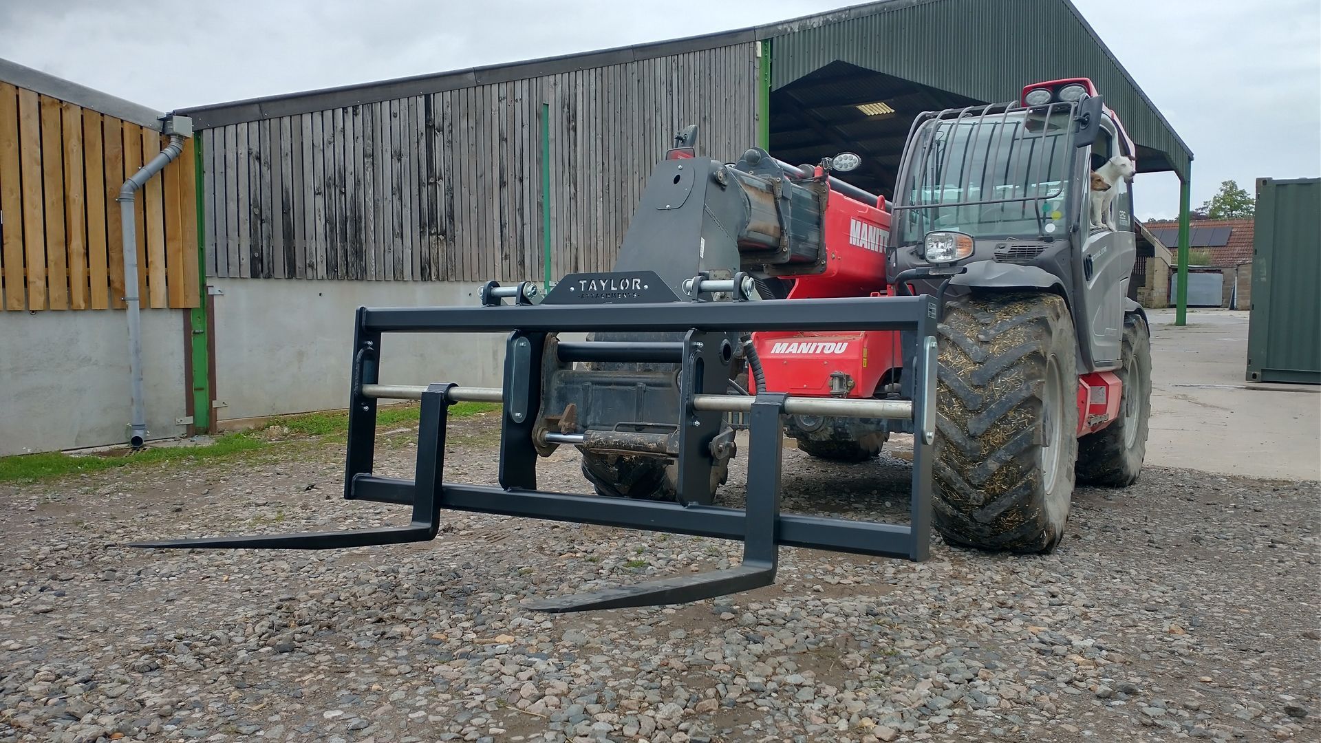 A red tractor with a forklift attached to it is parked in a gravel lot.