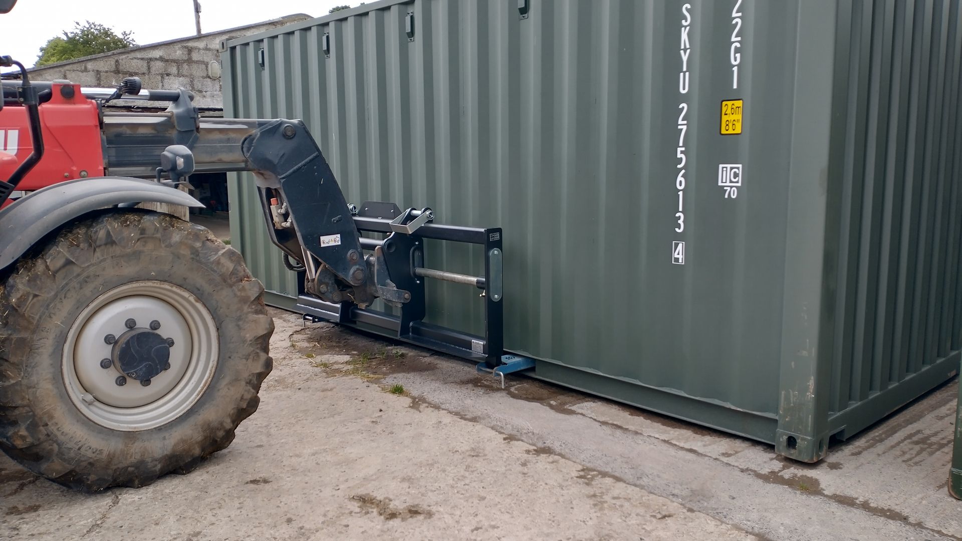A red tractor is driving next to a green shipping container.