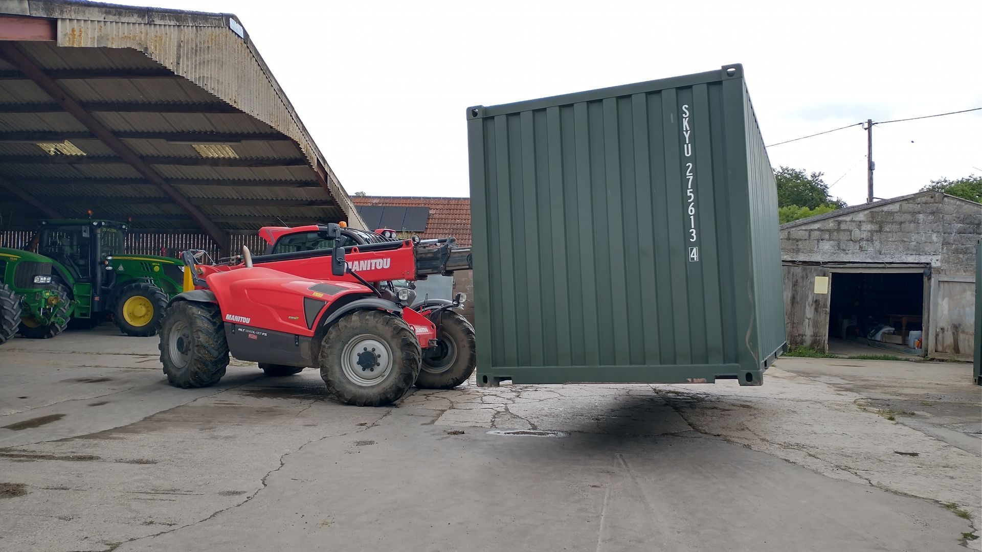 A red forklift is carrying a green shipping container.