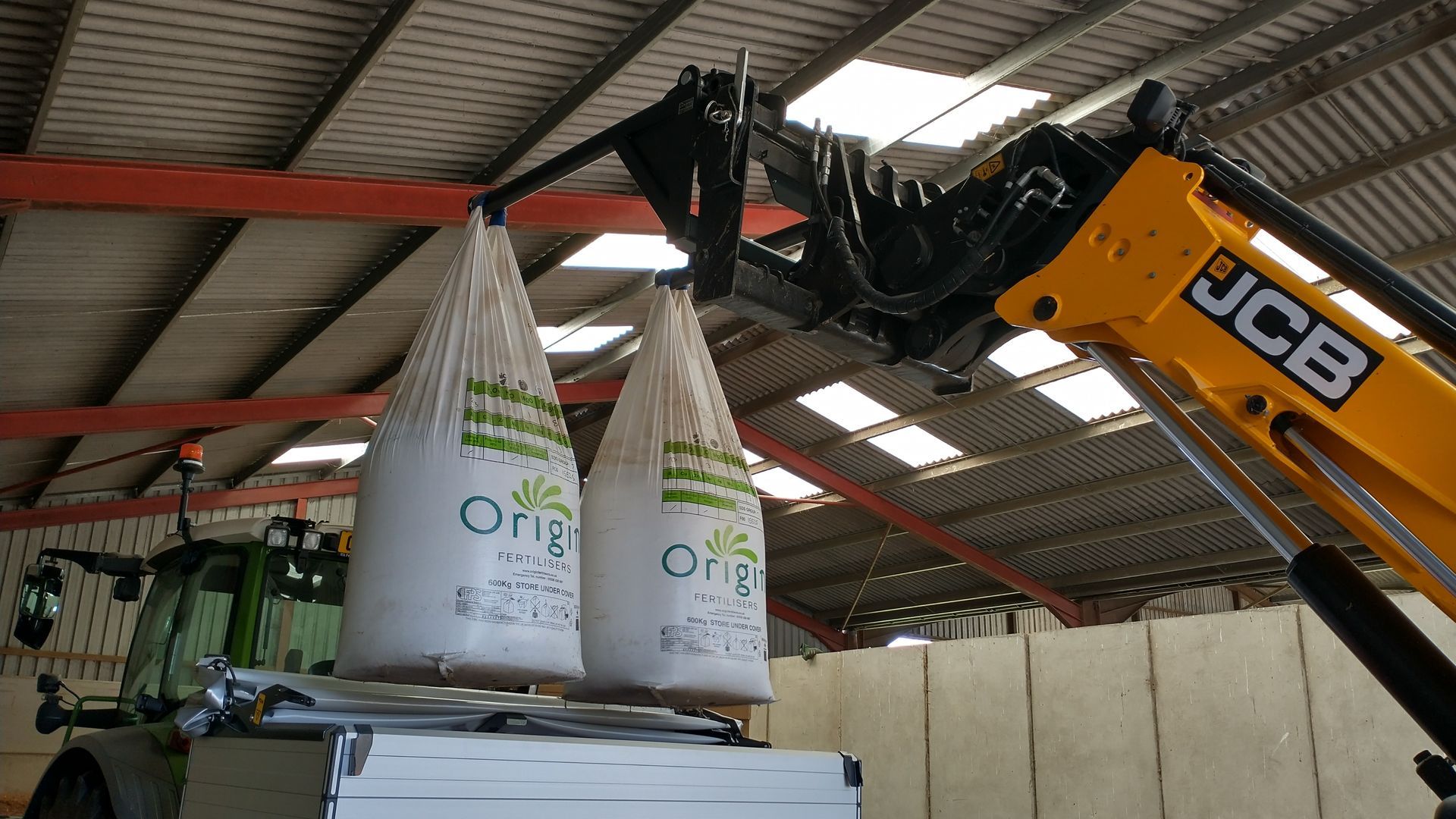 A jcb crane is lifting two bags of rice on top of a truck.