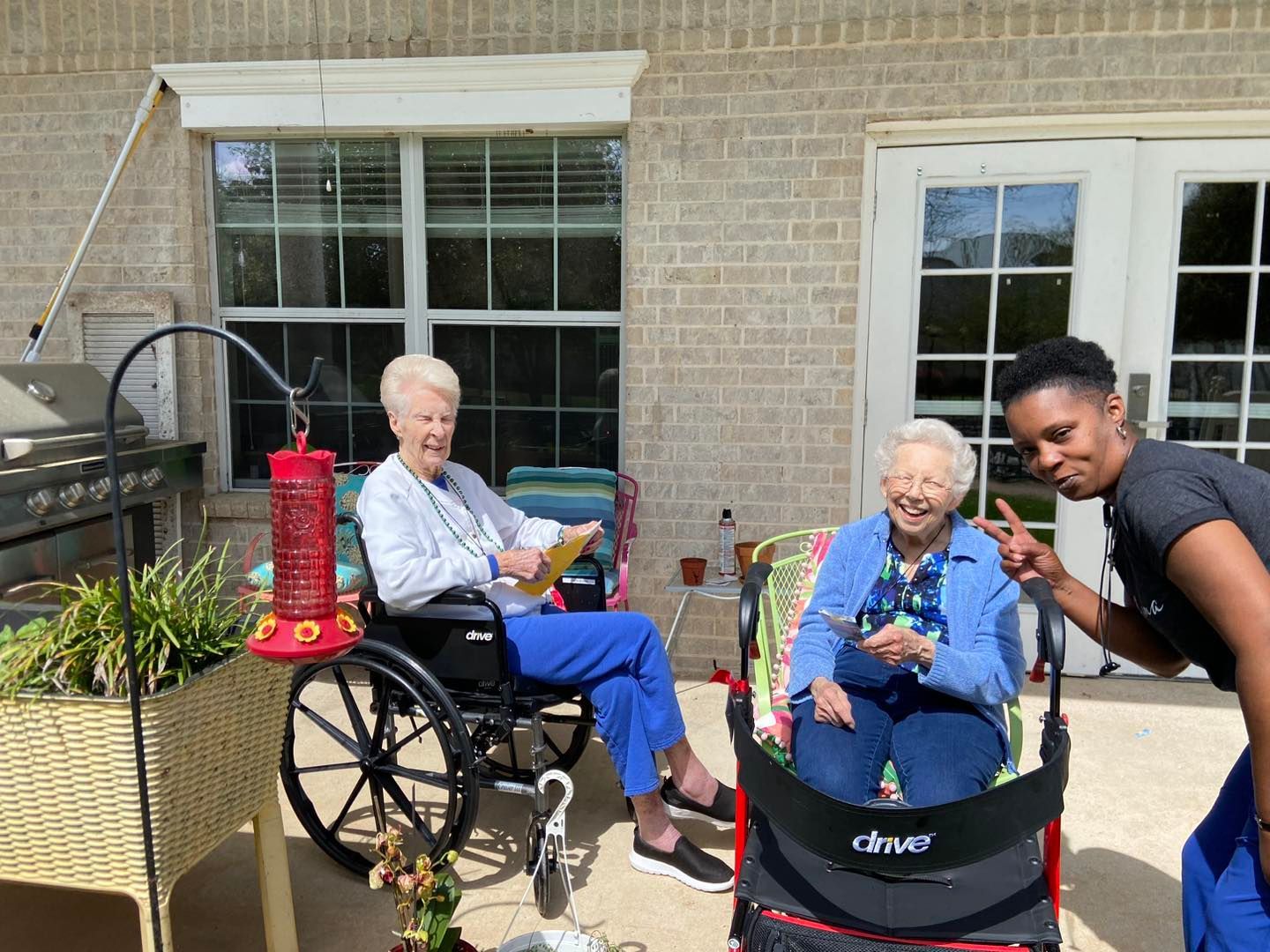 Two elderly women in wheelchairs are sitting on a patio with a nurse.