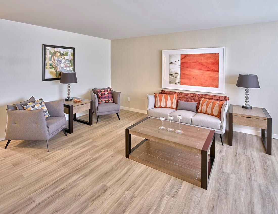 A bright living room with gray seating, a wooden coffee table, two side tables with lamps, and framed wall art.