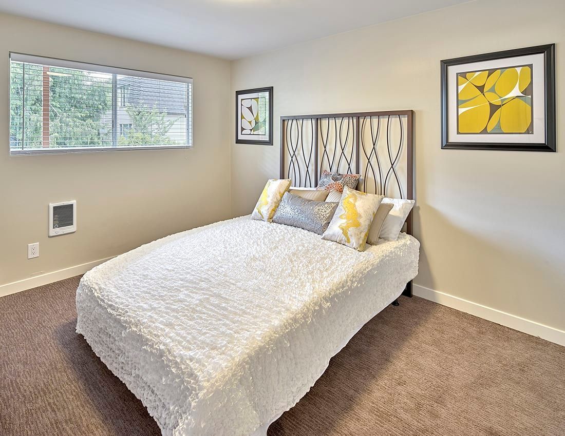 A bedroom with a white textured bed, patterned headboard, and two framed art pieces on light beige walls.