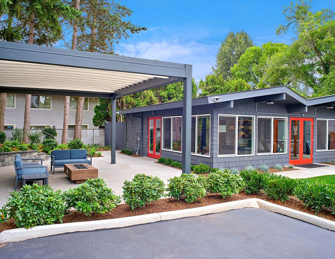 A dark gray mid-century modern building with orange doors, a patio with seating, and a modern pergola under a blue sky.
