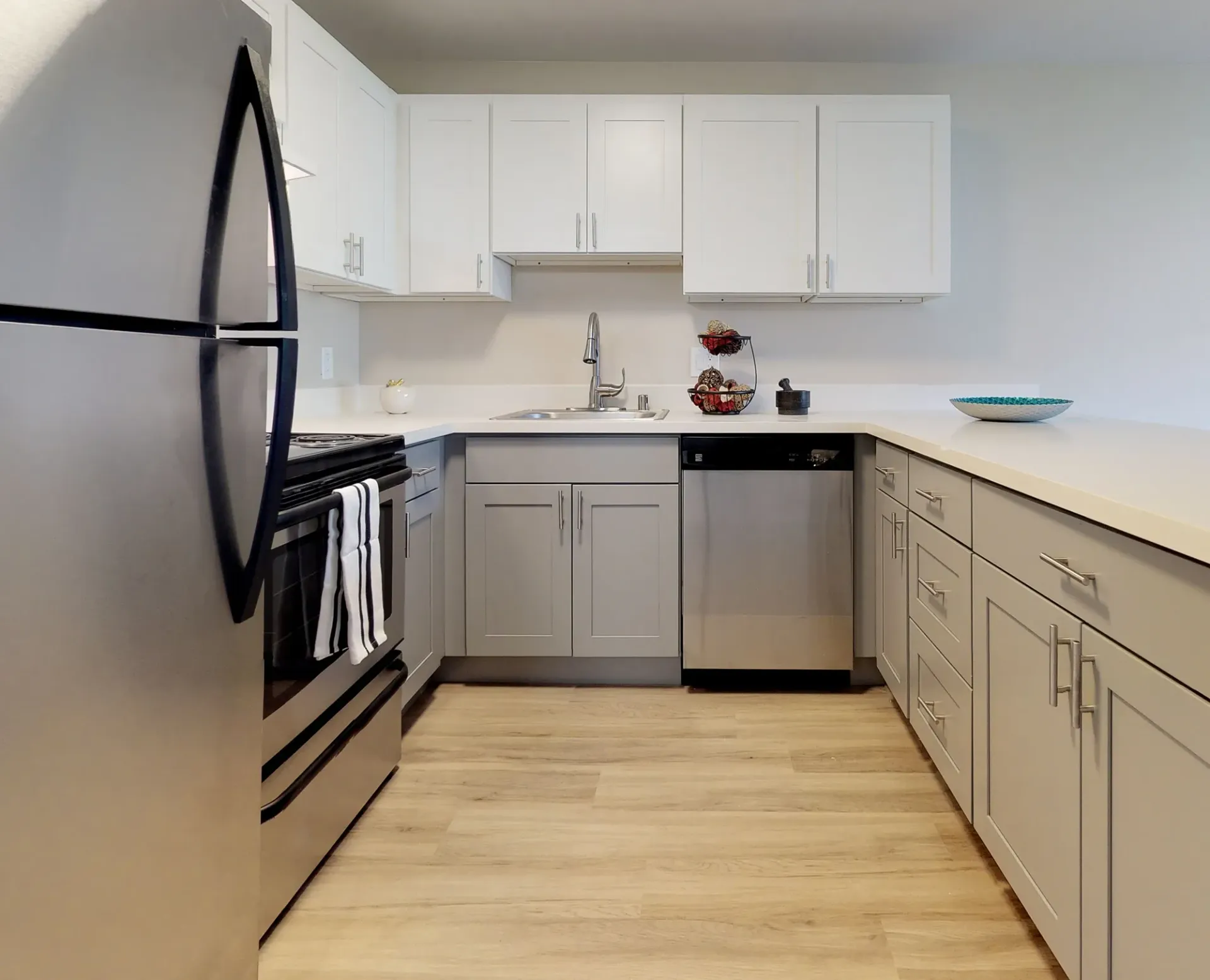 A modern kitchen featuring white upper cabinets, light gray lower cabinets, stainless steel appliances, and wood flooring.