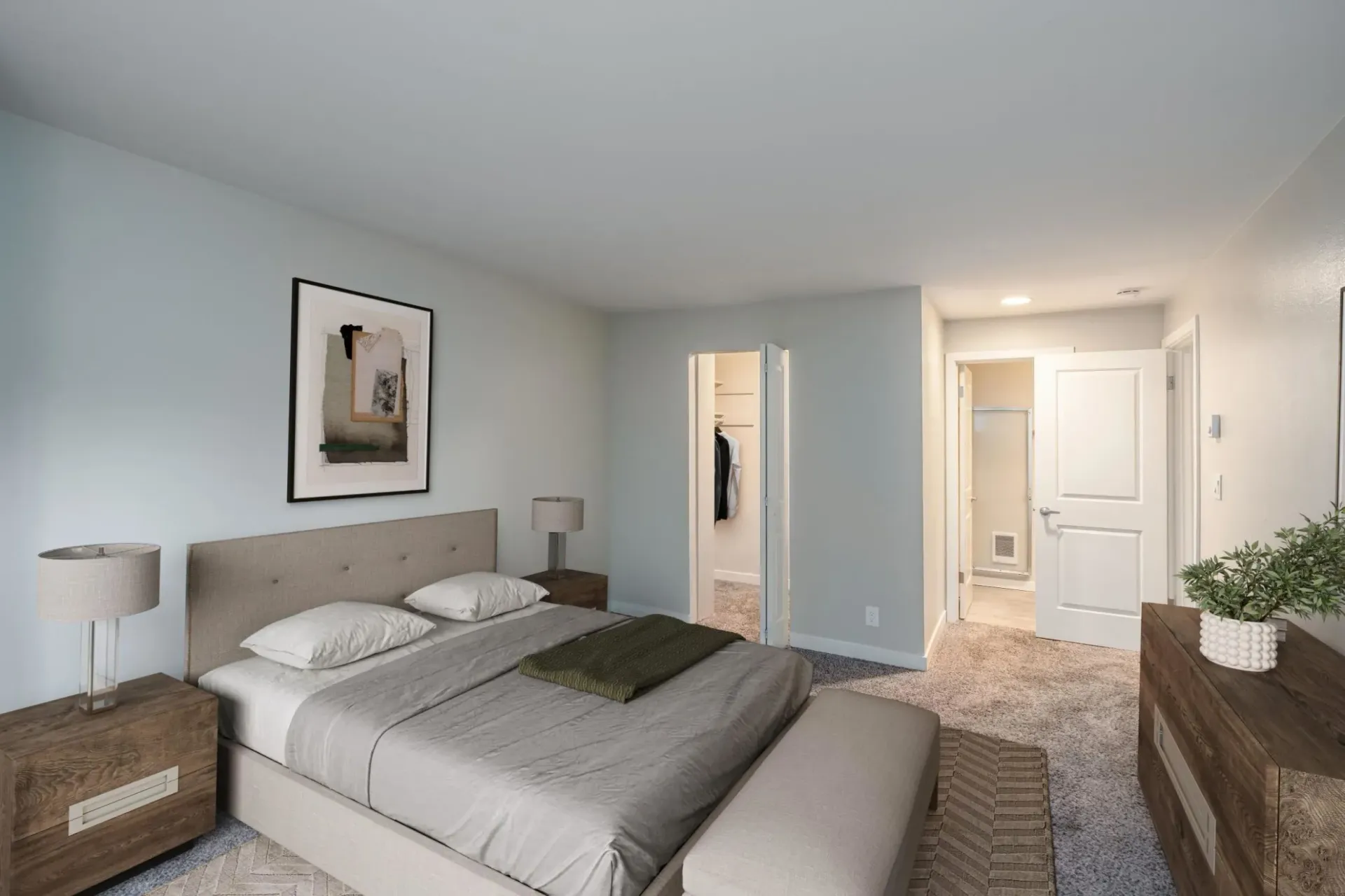 A light-walled bedroom featuring a queen bed with gray bedding, two wood nightstands, and a doorway to a walk-in closet.