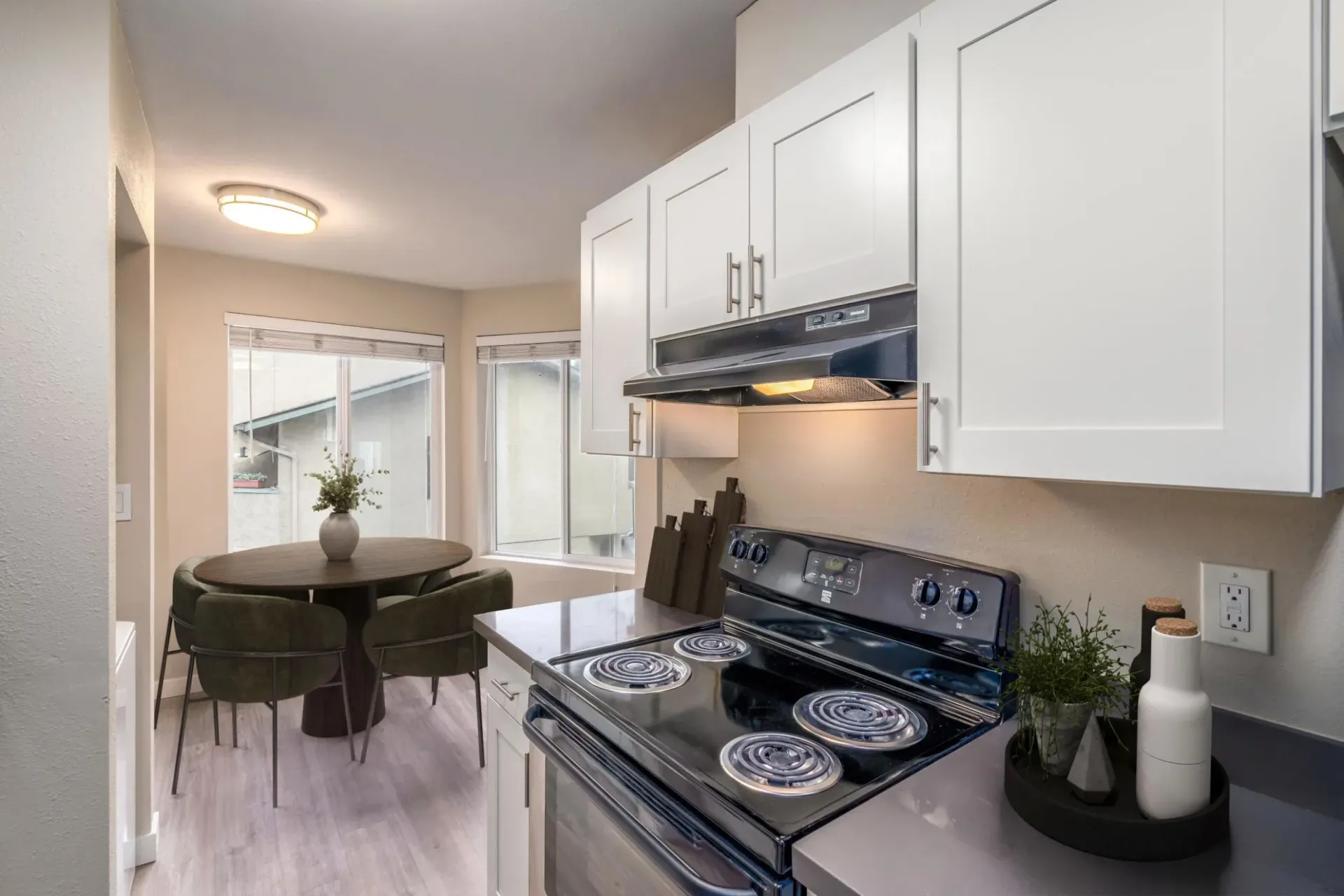 A bright, modern kitchen featuring white cabinets, a black stove, and a dining table with chairs by a window.