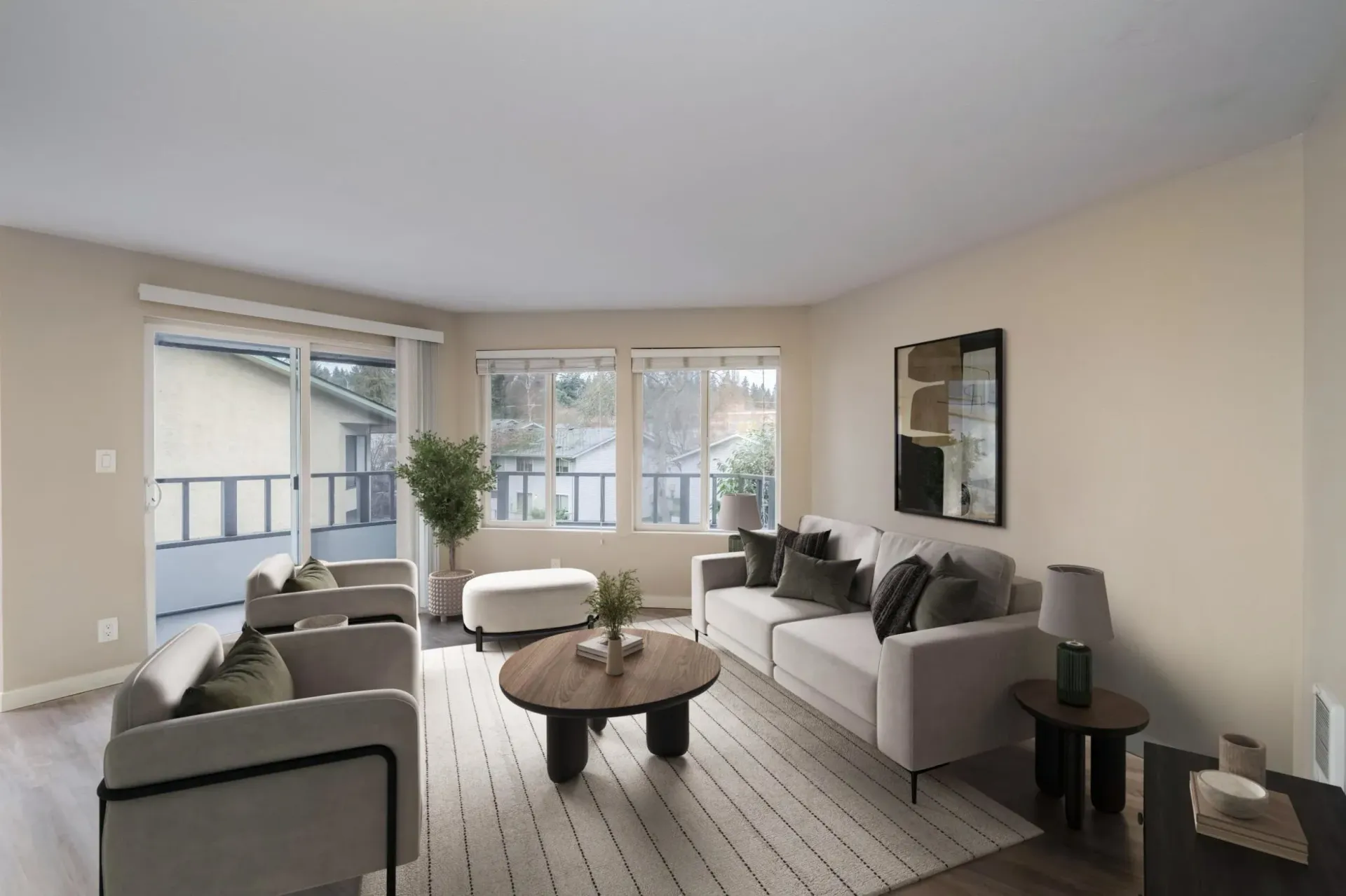 A light-toned living room featuring a sofa, two armchairs, a round coffee table, and a rug facing windows to a balcony.