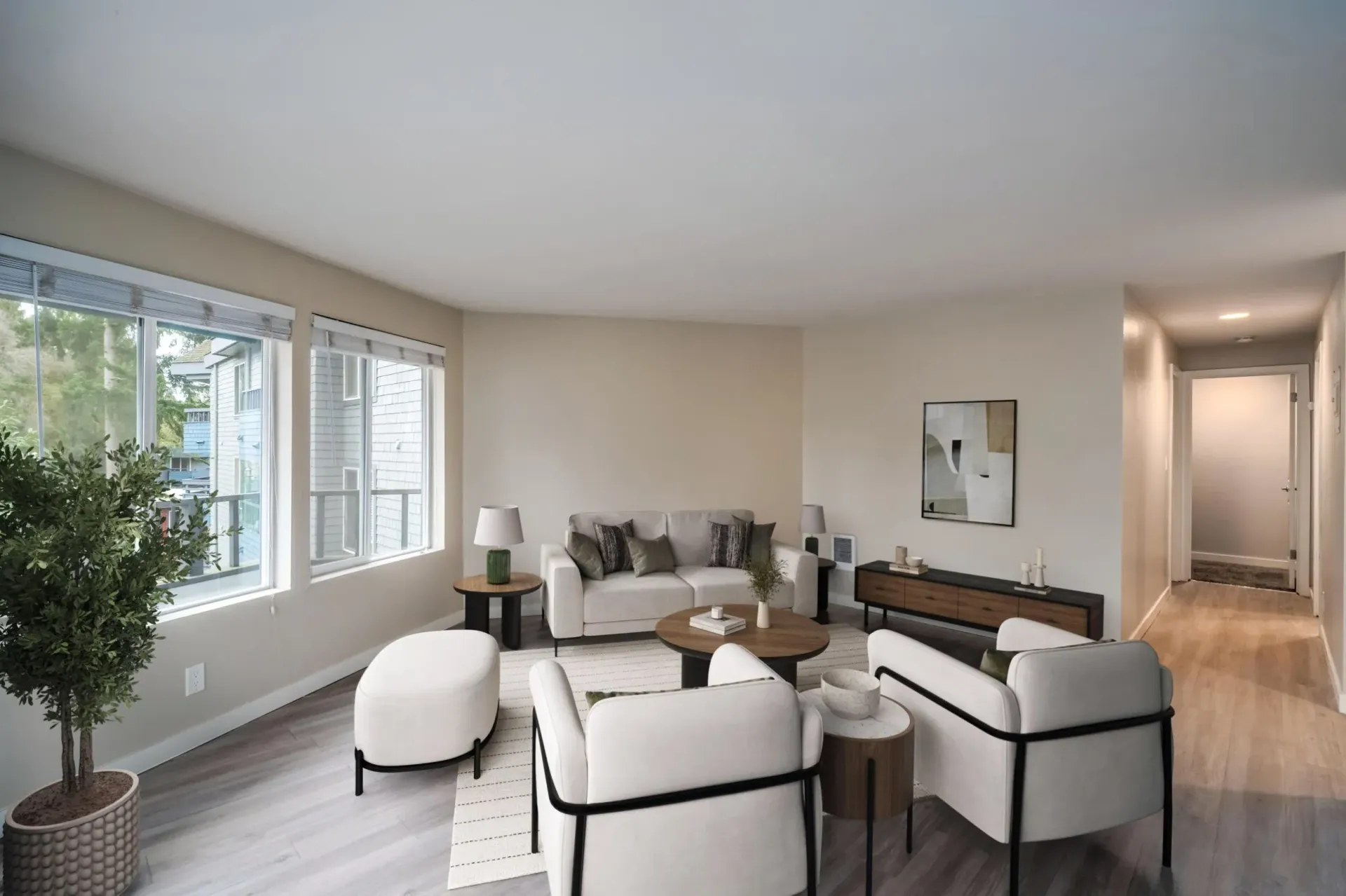 A neutral-toned living room featuring a white sofa, two armchairs, a round coffee table, and a large window with greenery.
