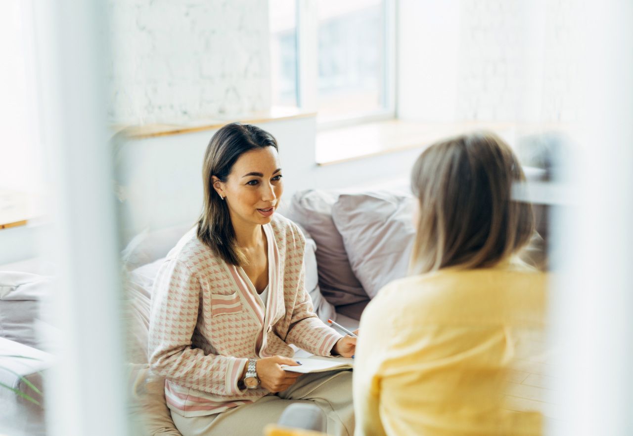 Two women are sitting on a couch talking to each other.