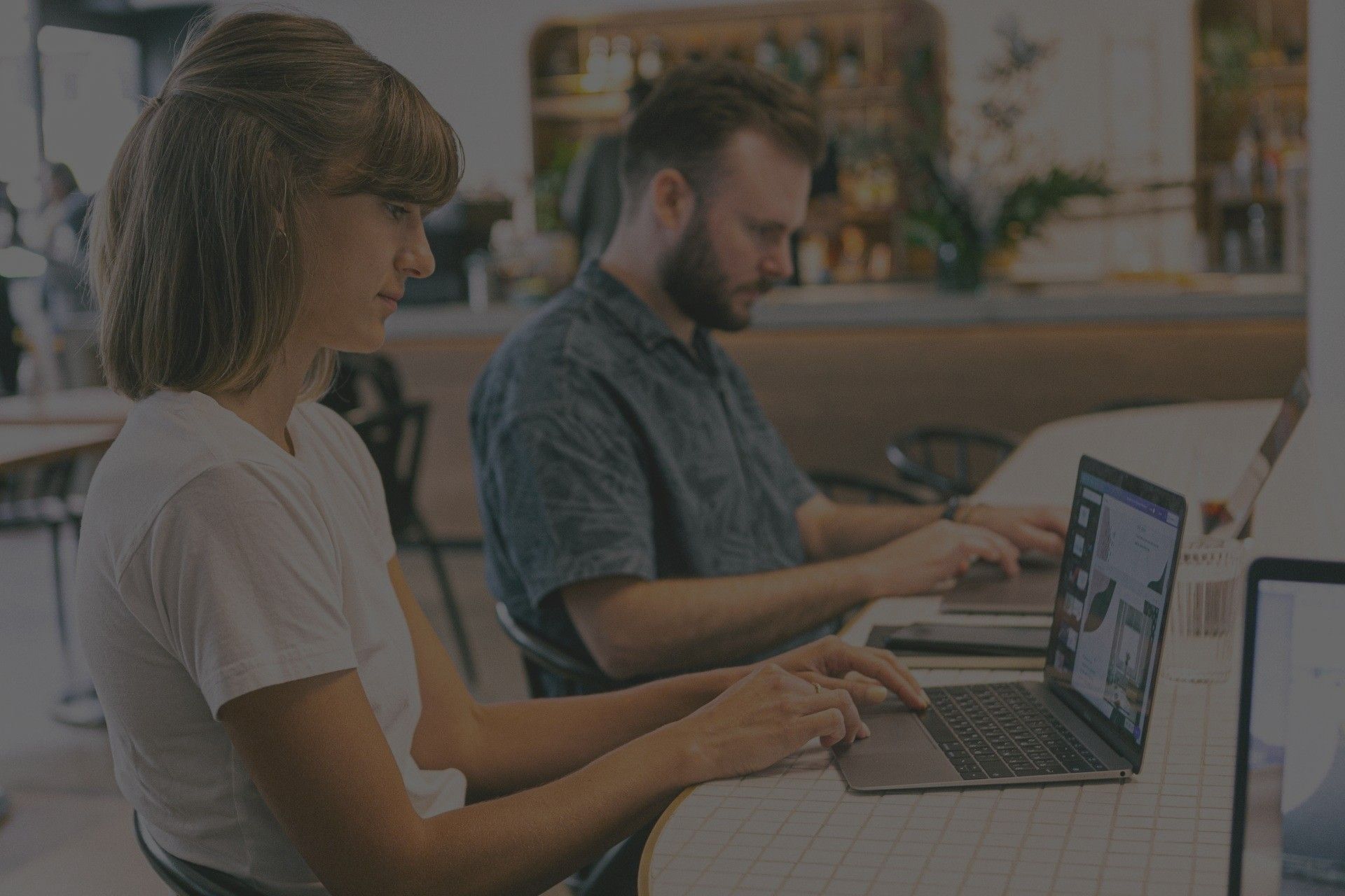 A man and a woman are sitting at a table using laptops.