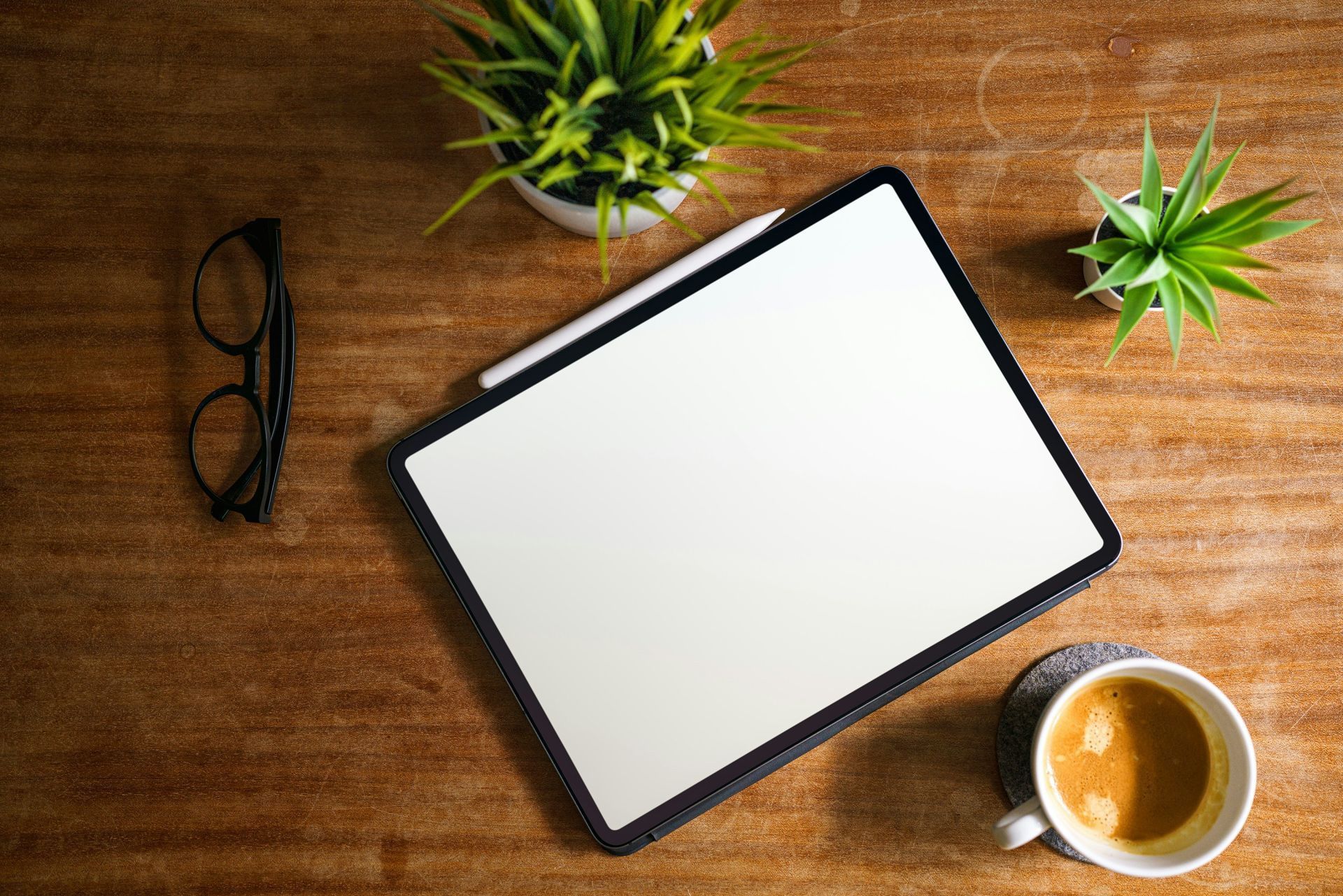 A tablet is sitting on a wooden table next to a cup of coffee and a plant.