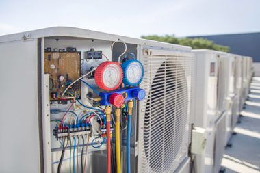 HVAC technician gauges attached to rooftop air conditioner unit with exposed wiring and fan