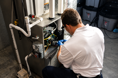 Technician kneeling and working on open HVAC unit with tools in a utility room