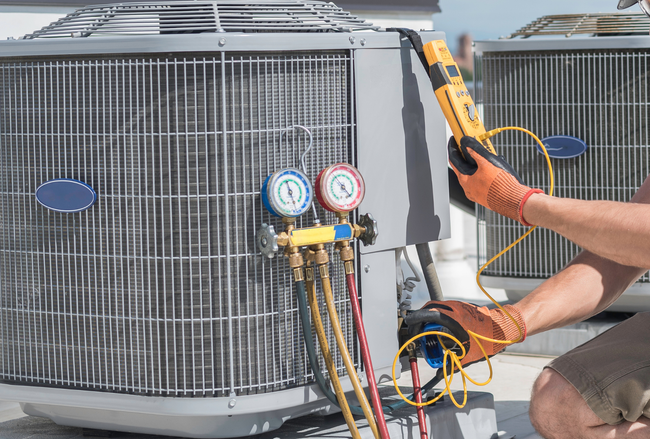 Technician using gauge manifold to service an outdoor HVAC condenser unit with tools and hoses attached