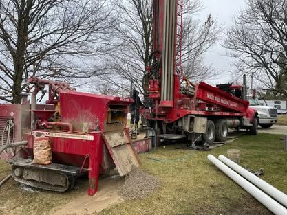 A Red Truck Is Parked In A Grassy Field Next To A Drilling Rig - Union City, IN - Wiley Well Drilling