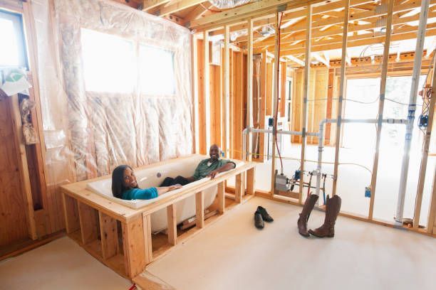 A man and a woman are laying in a bathtub in a house under construction.