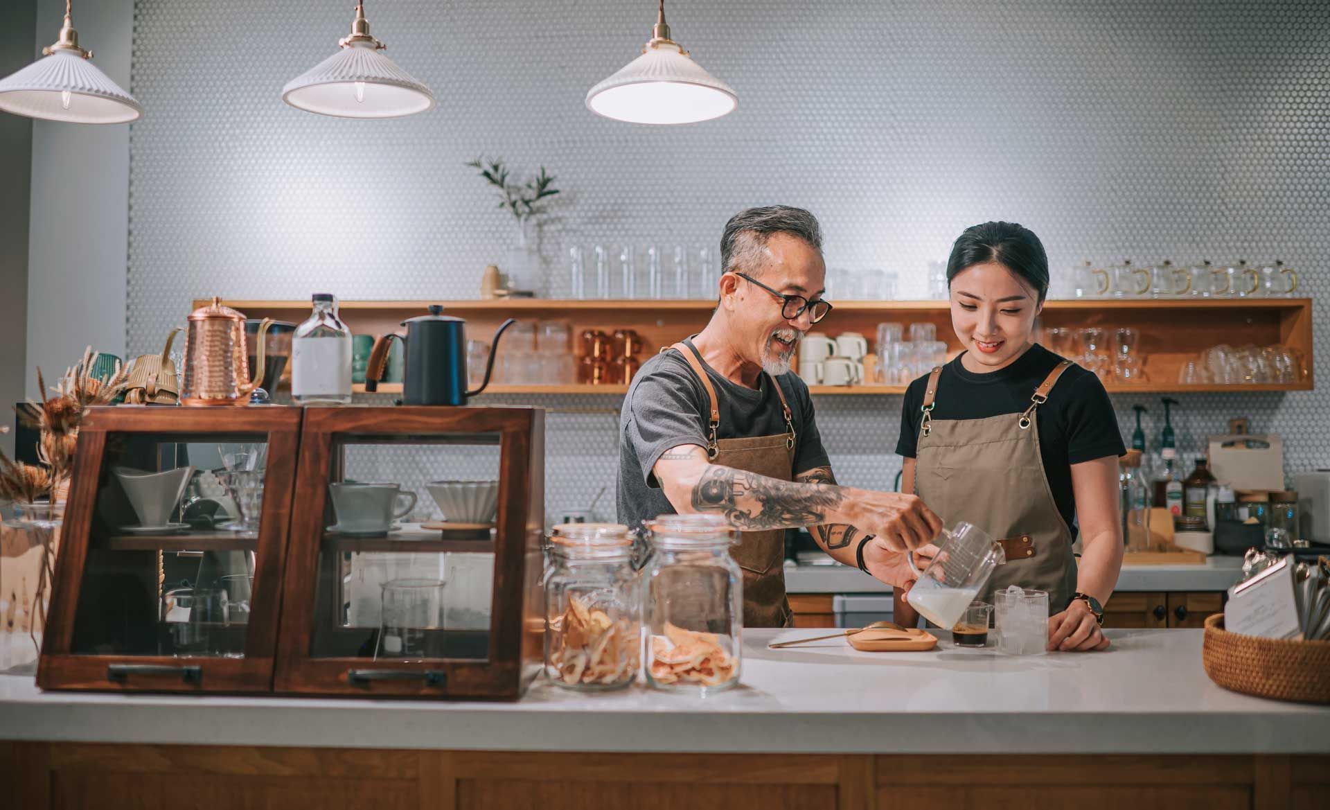 Two baristas prepare coffee behind a counter in a cafe.