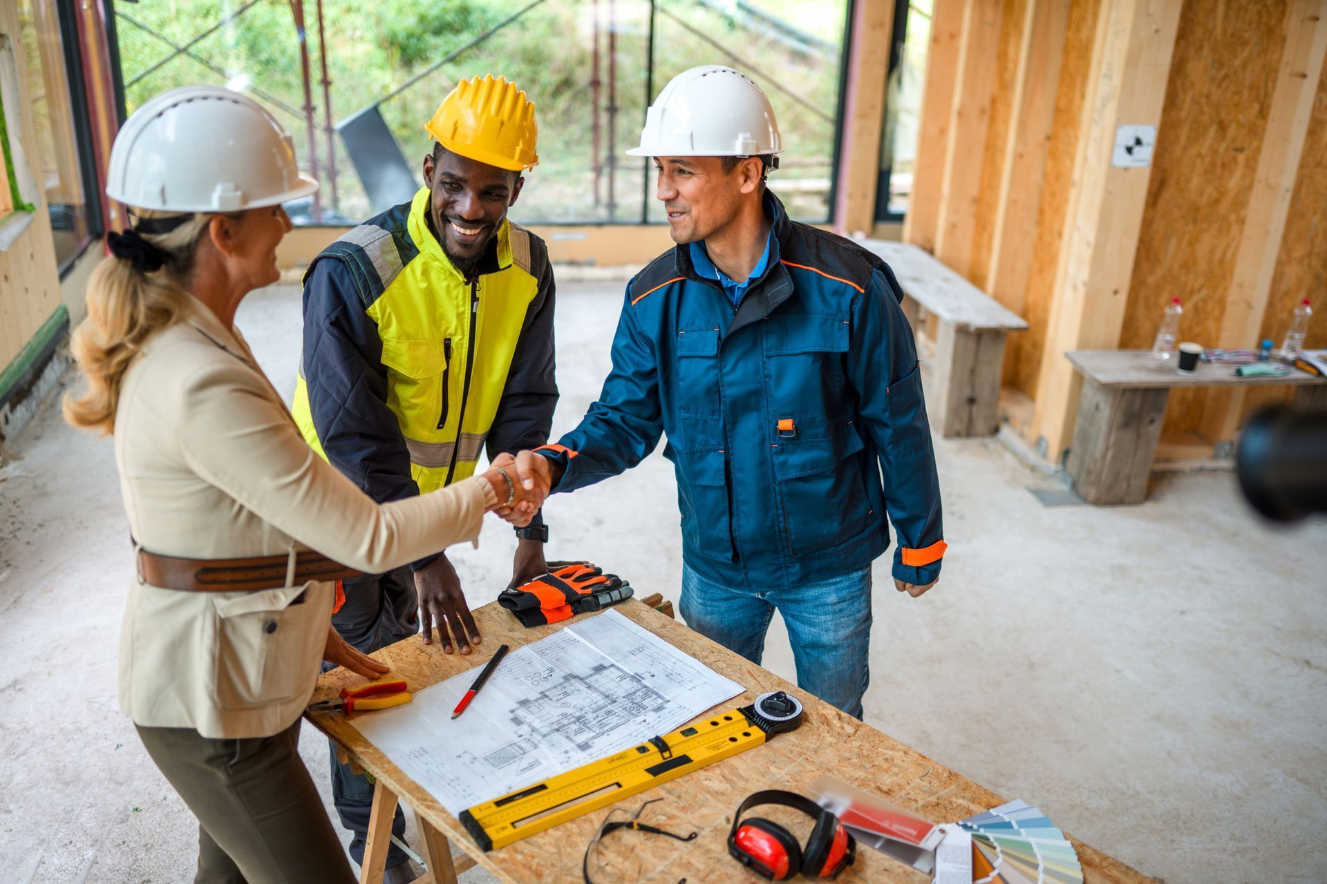 Construction workers and a woman in business attire shaking hands over a blueprint at a construction site.