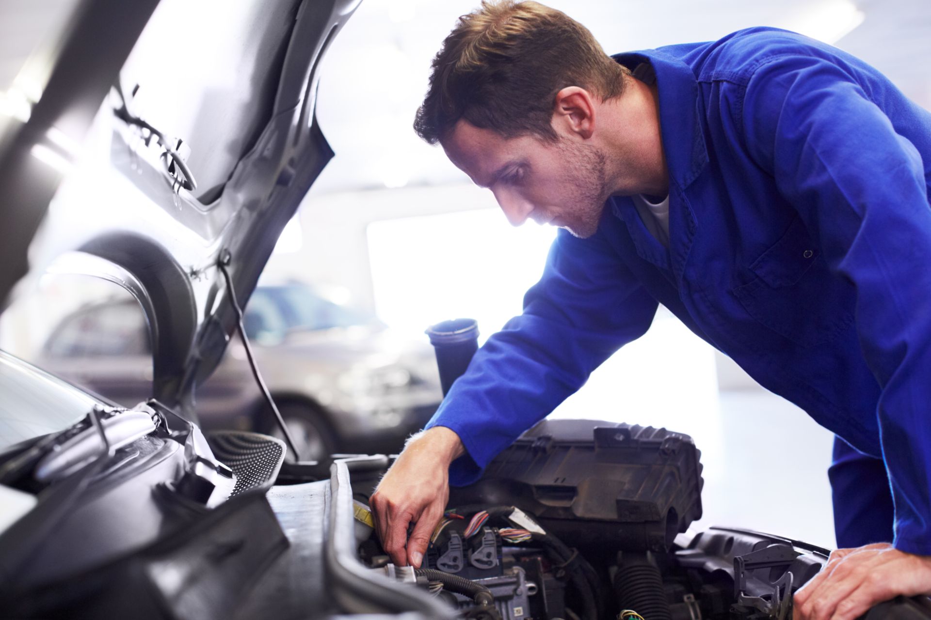 Mechanic in blue jumpsuit examining car engine in a garage.
