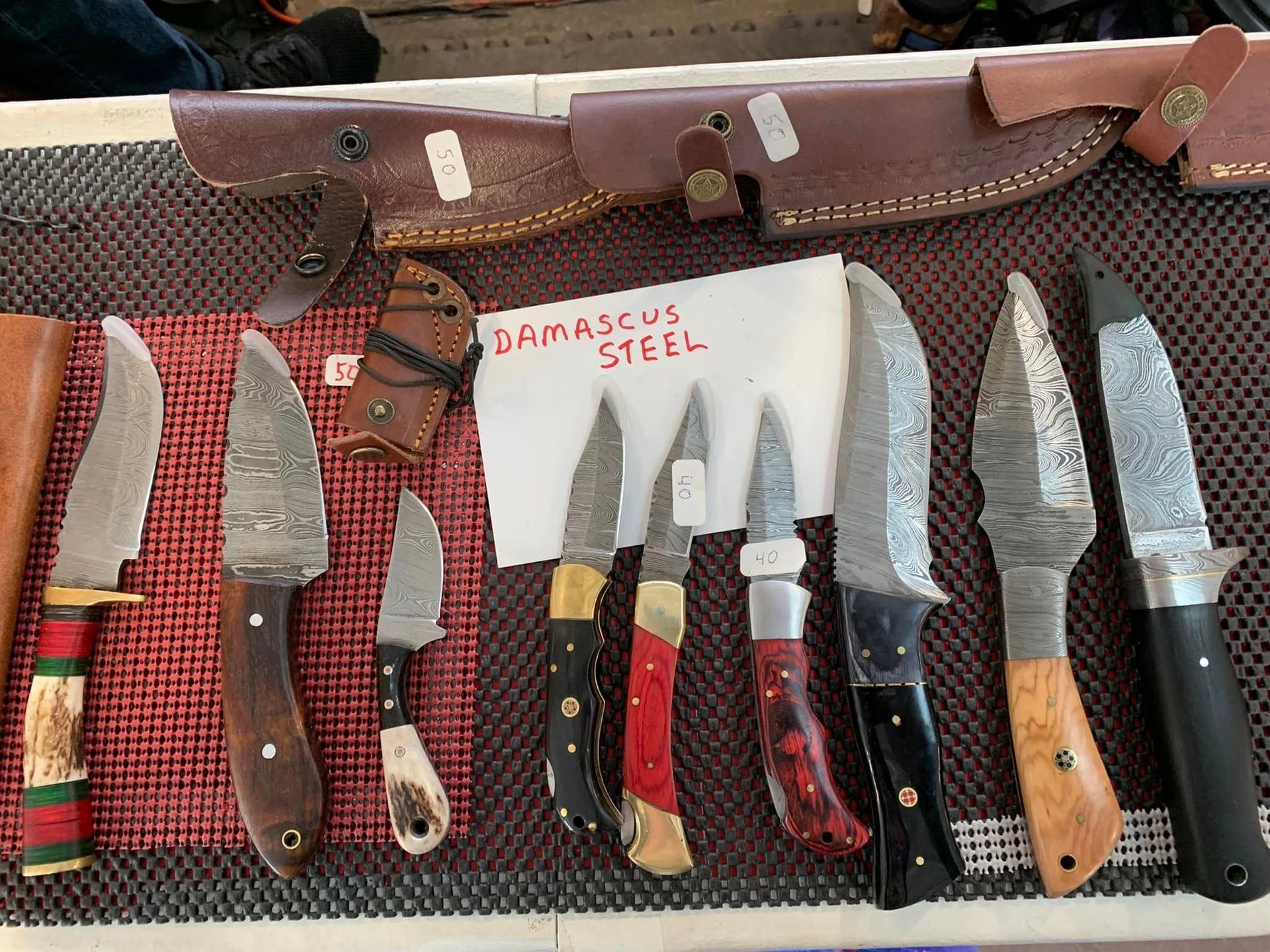 Display of various Damascus steel knives with leather sheaths.