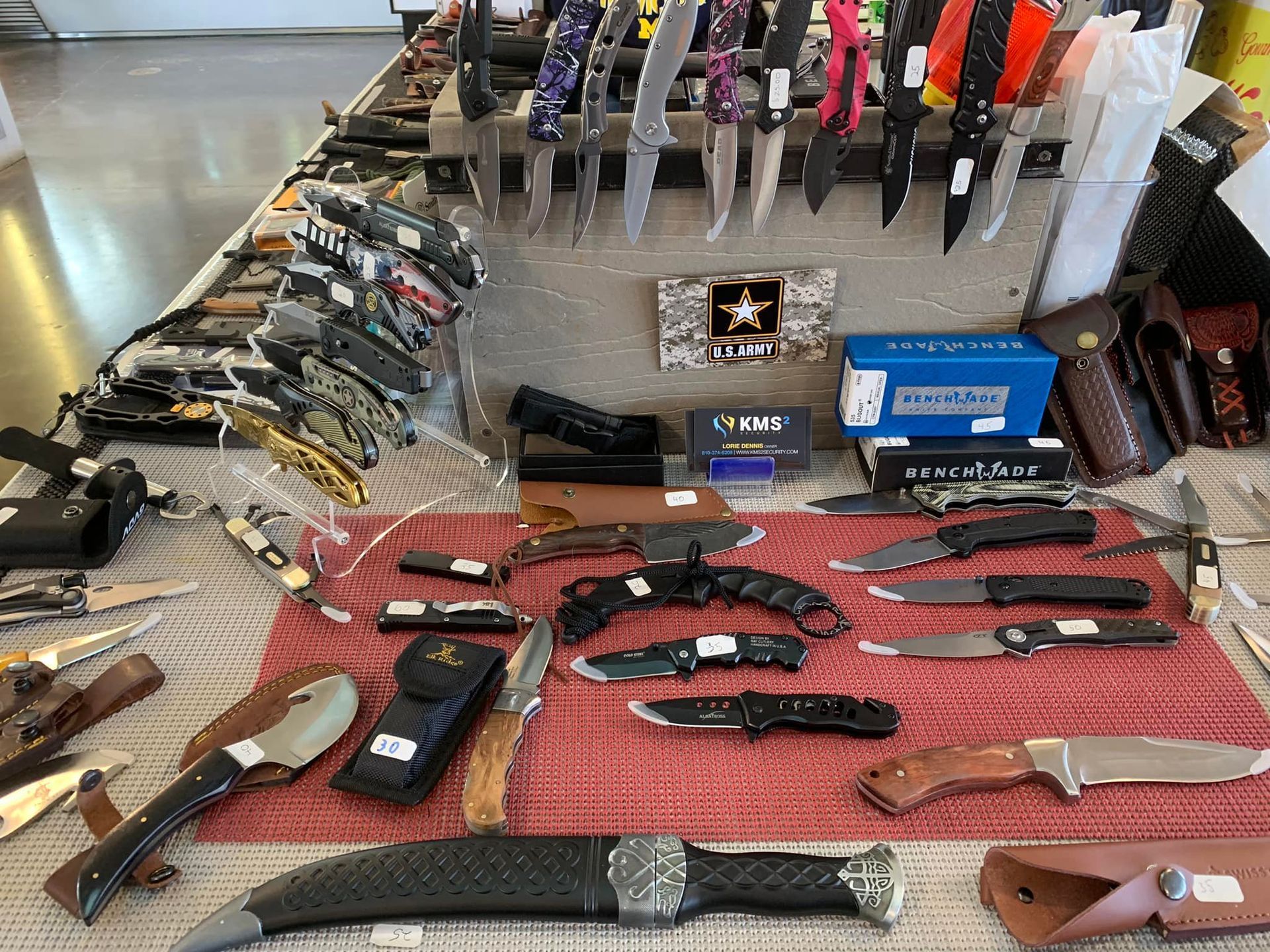 Display of various knives on a table; some in sheaths, some on a rack.