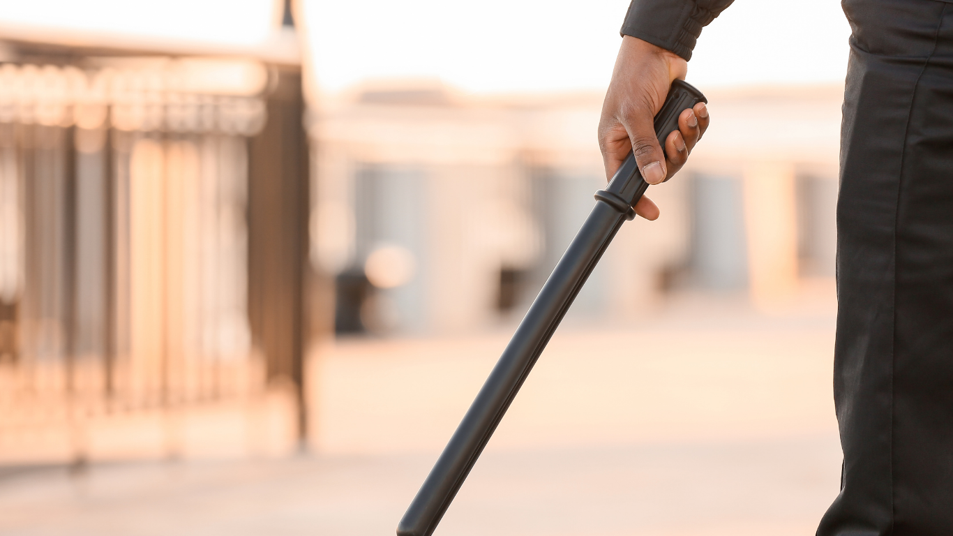 Person holding a black baton outdoors near a fence.