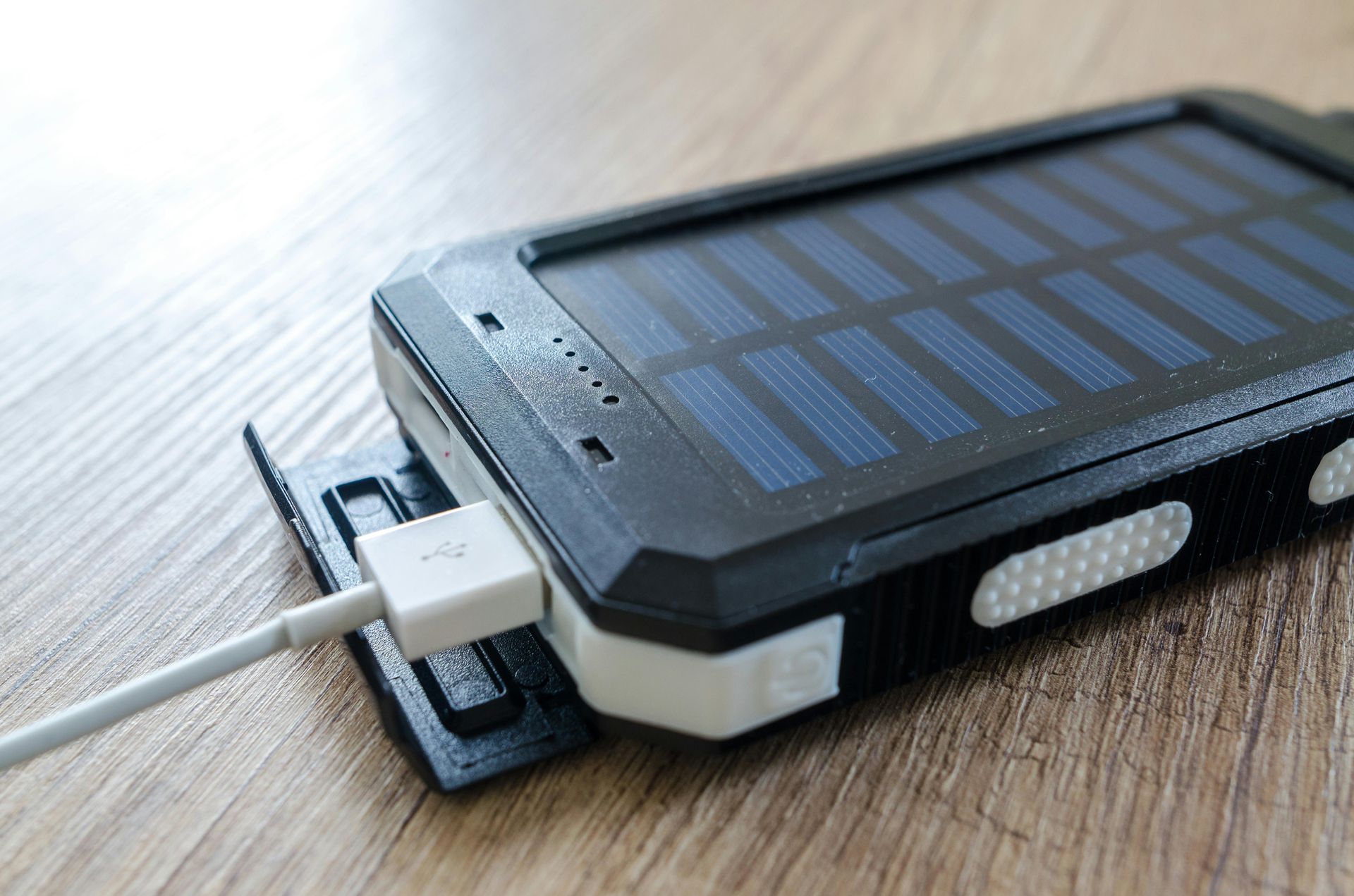 Black and white solar-powered charger with USB cable plugged in, resting on a wooden surface.