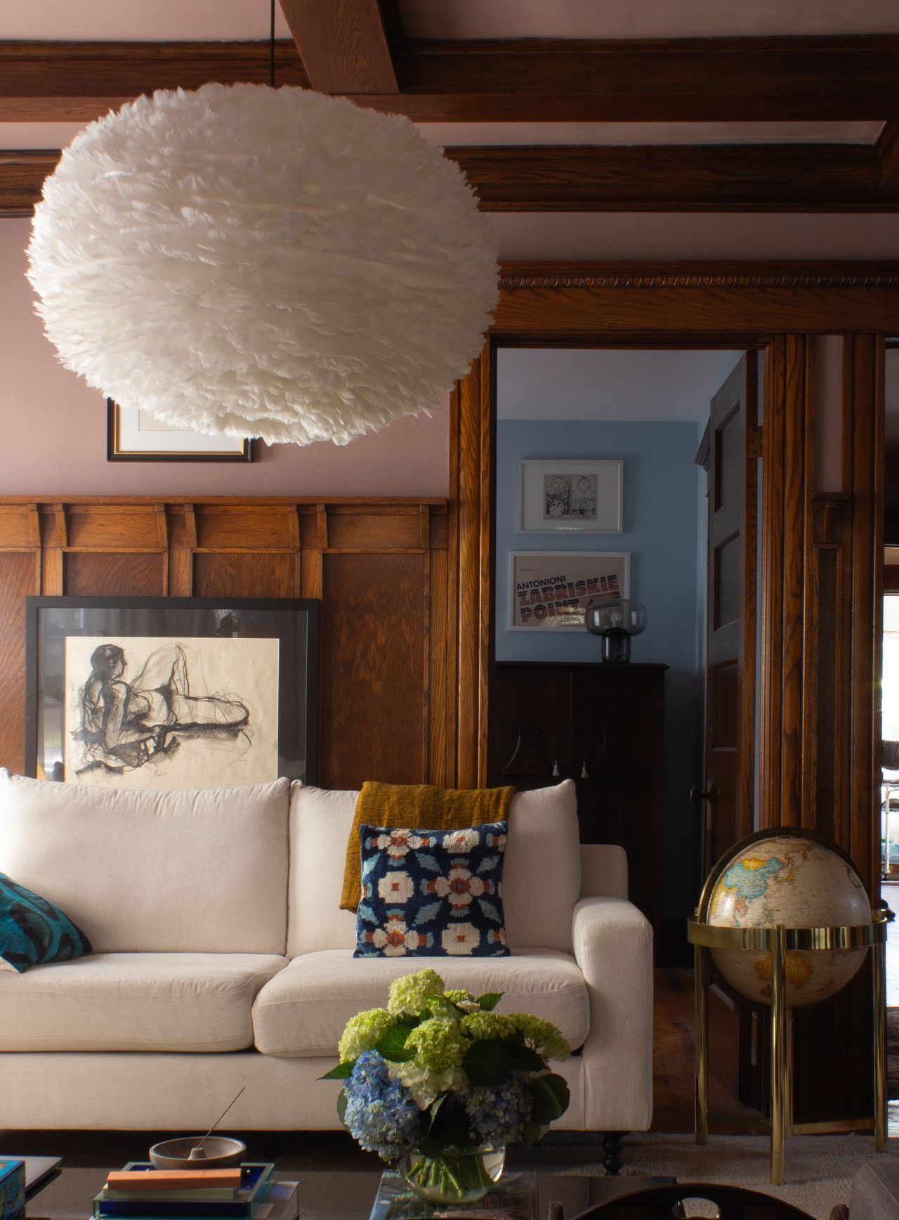 An arts and crafts living room with original oak paneling and a large feather pendant light.