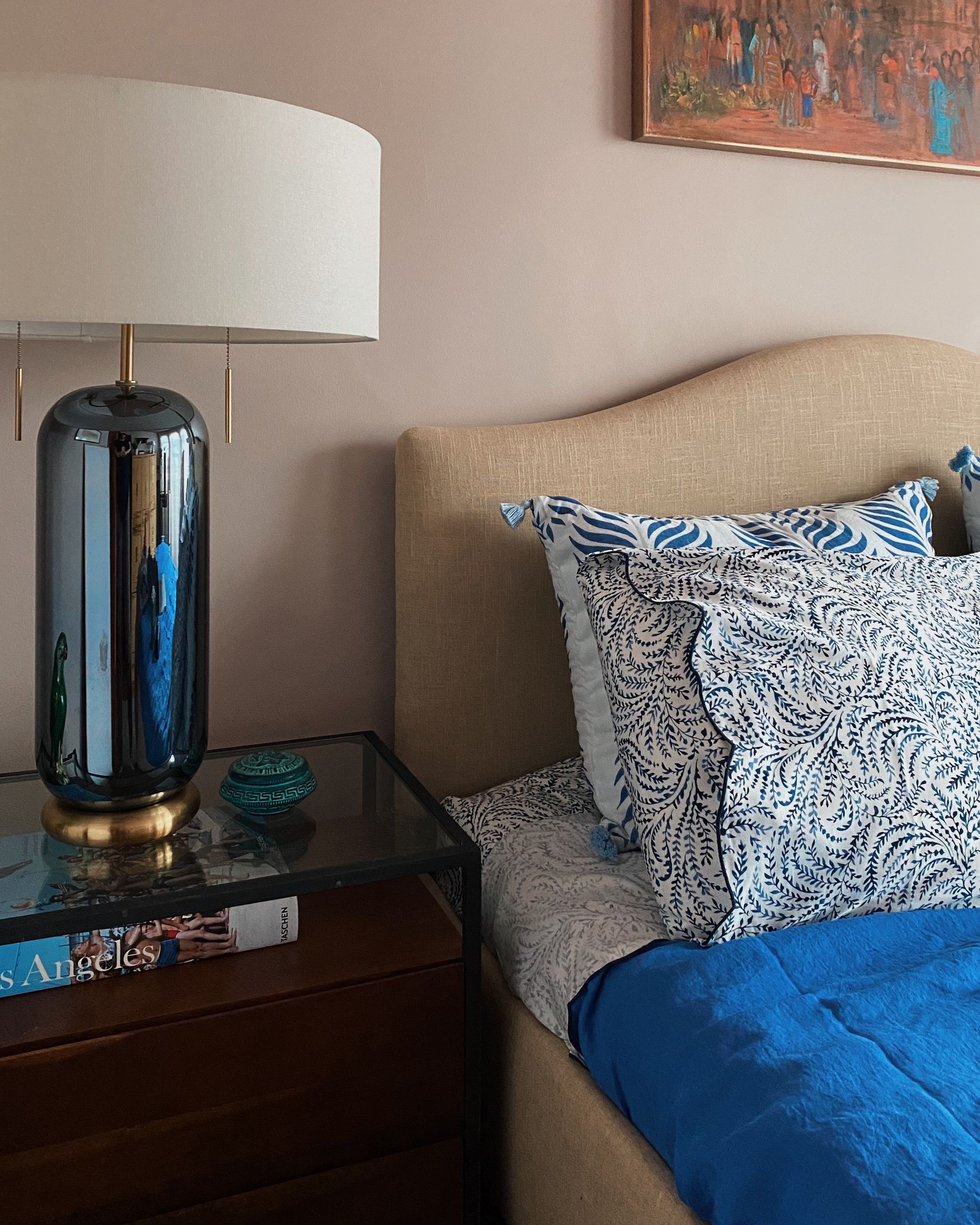 A bedroom with a blue iridescent table lamp and glass nightstand.